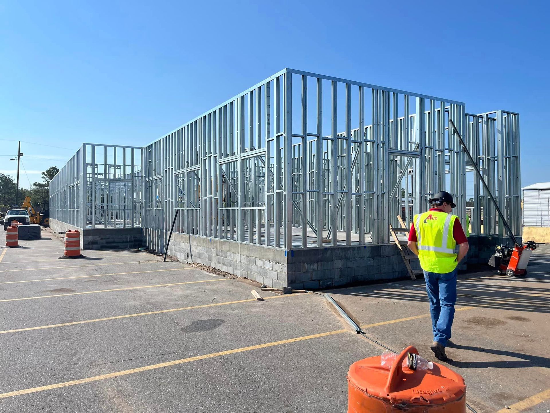 A man in a yellow vest is walking in front of a building under construction.