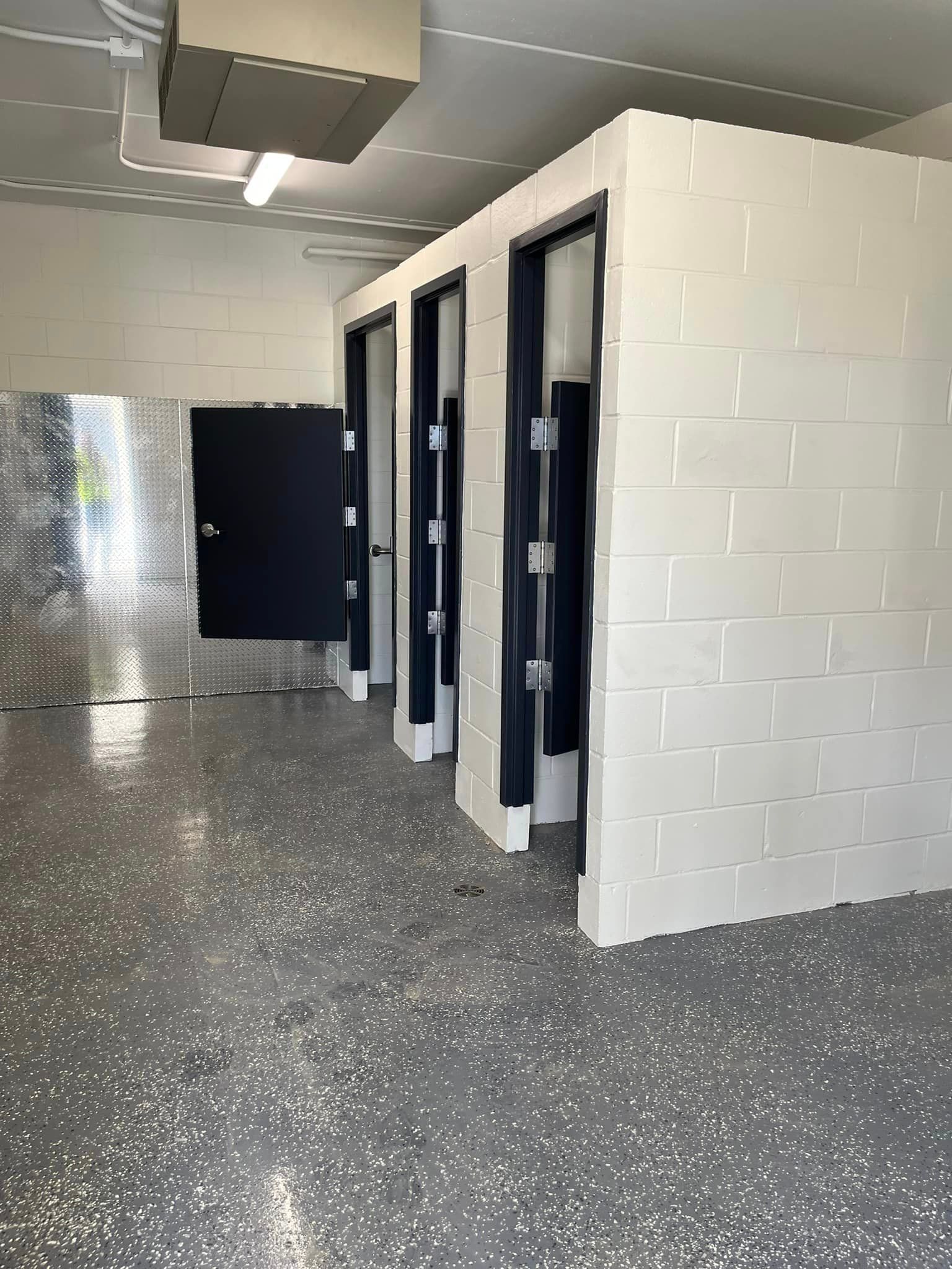 A bathroom with a row of cubicles and a gray floor.