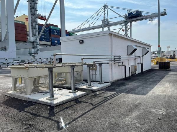 A white building with a lot of pipes and a crane in the background.