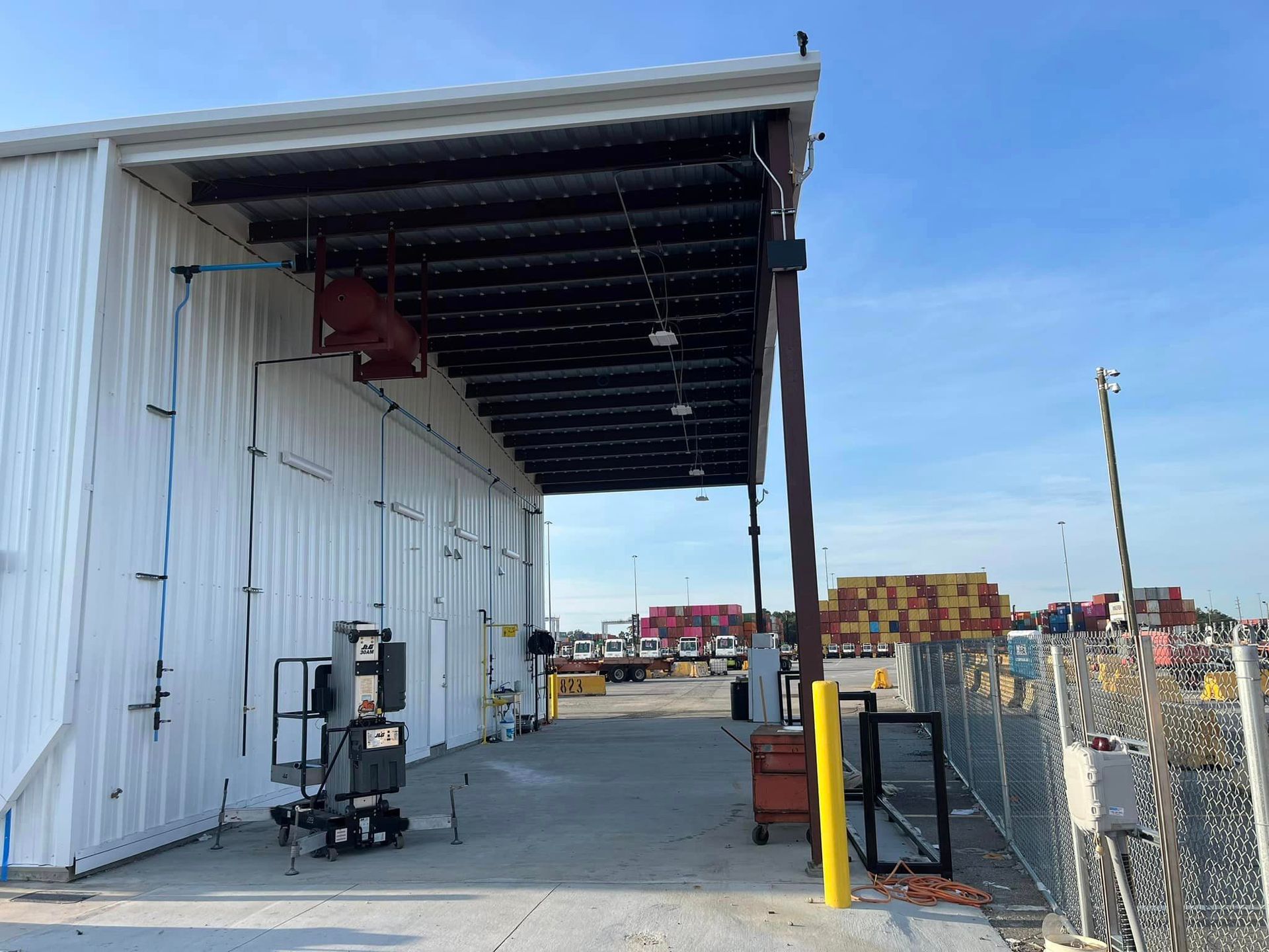 A large white building with a wooden roof is surrounded by a chain link fence.