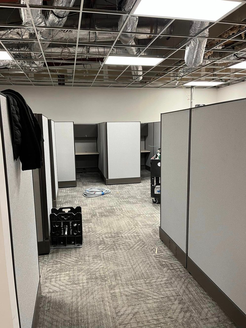 A hallway in an office with cubicles and a basket on the floor.