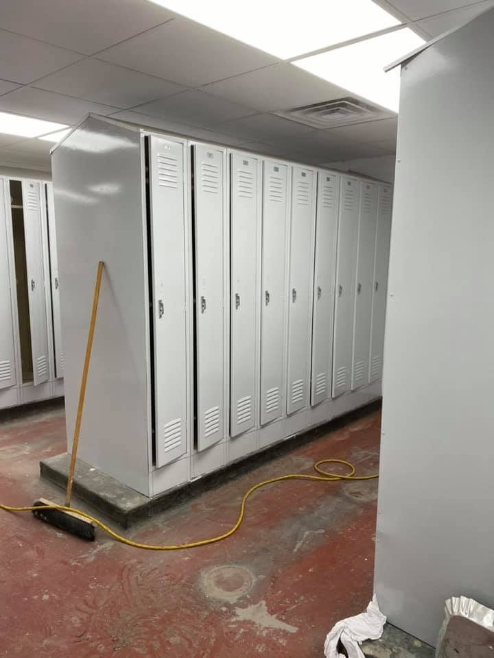 A room filled with lots of white lockers and a broom.