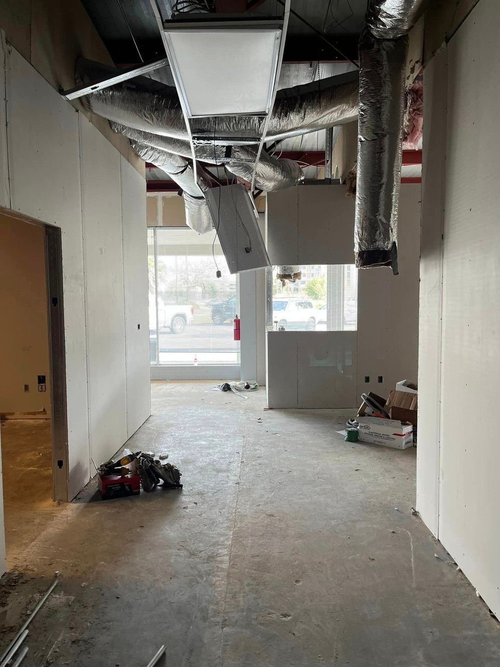 A hallway in a building under construction with ducts hanging from the ceiling.
