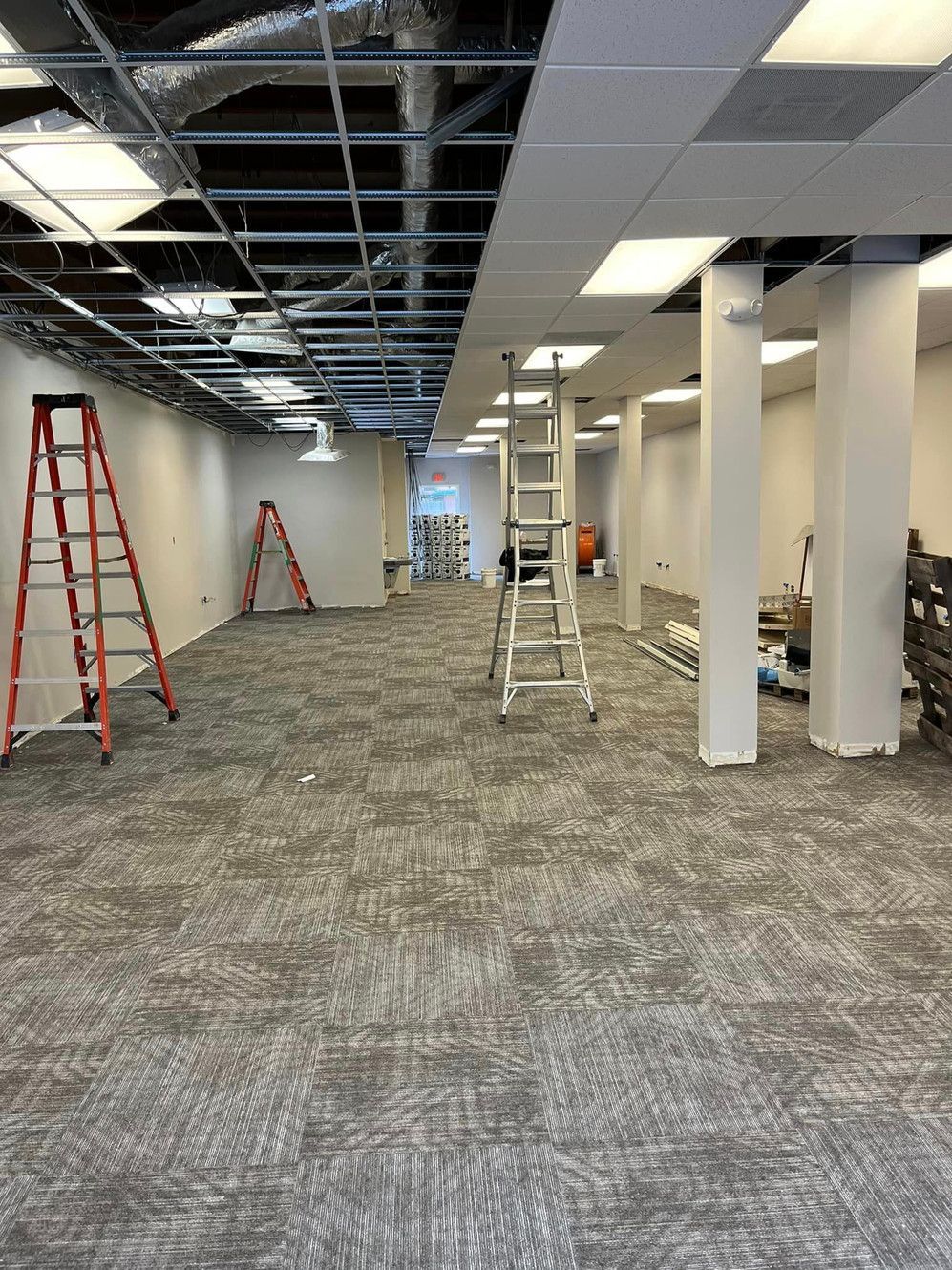A large room with a carpeted floor and a ladder in the middle of it.