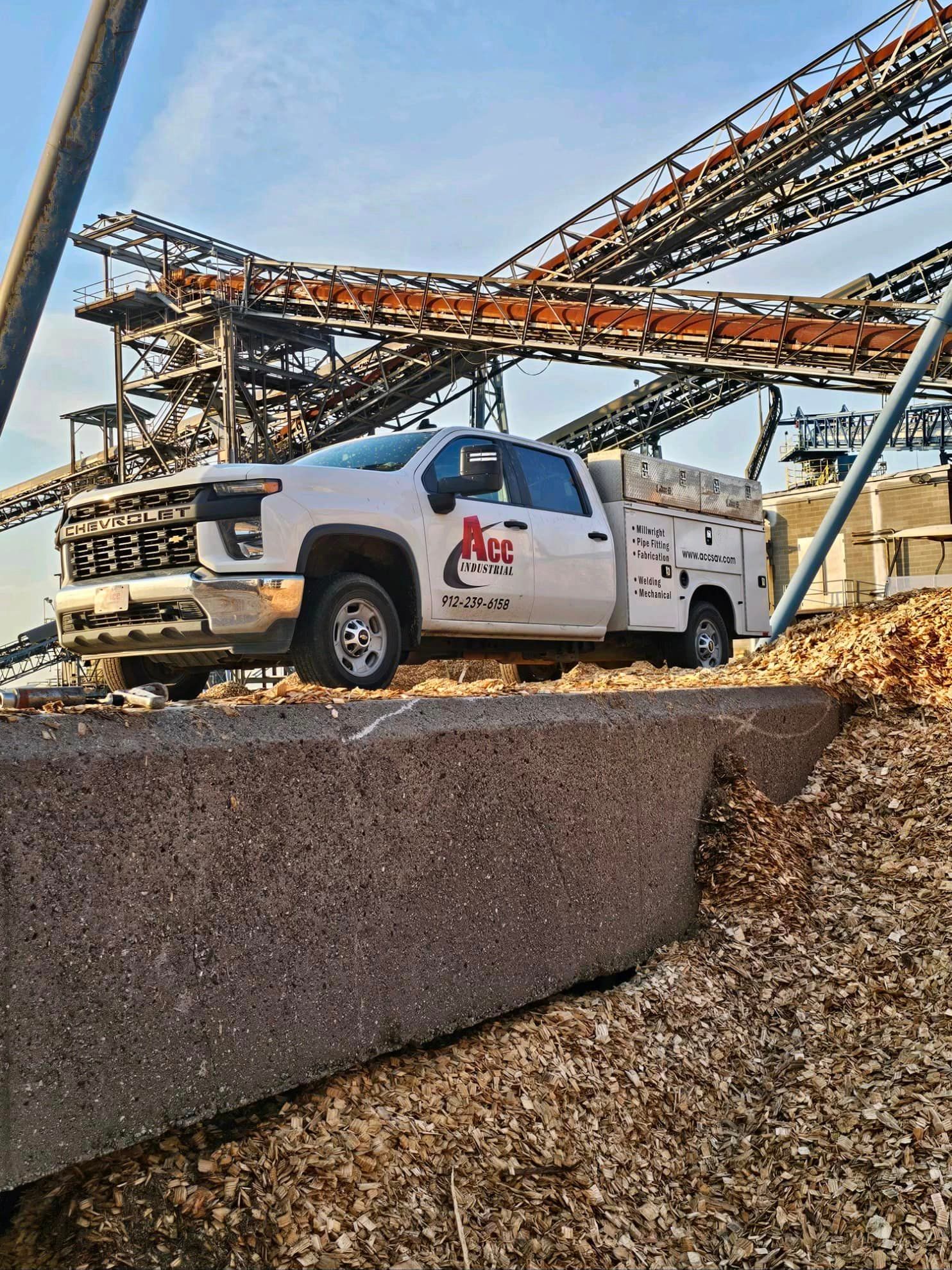 A white truck is parked on top of a pile of wood chips.
