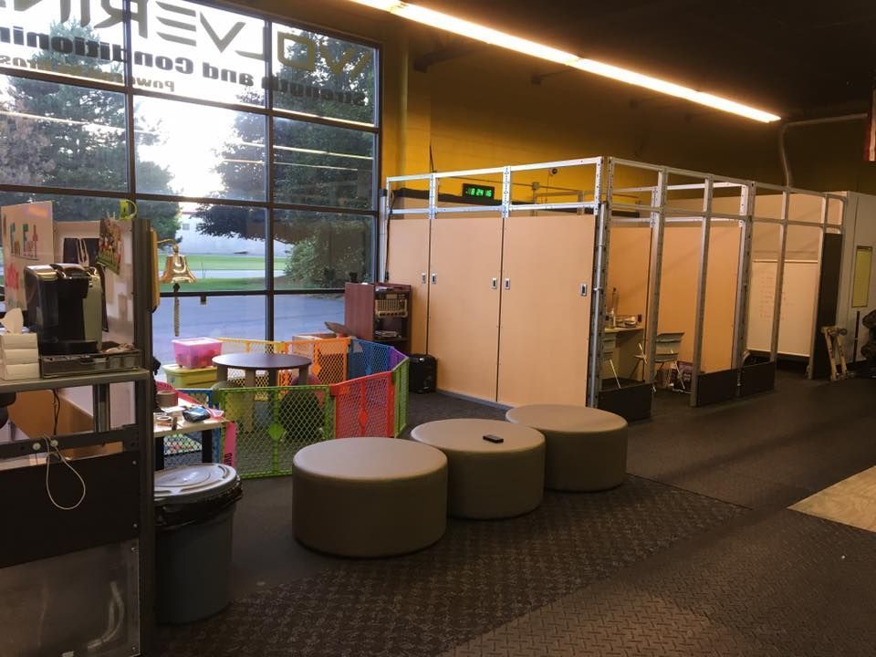 Interior of a gym with a children's play area, seating, and private workout stalls near a large window with an outdoor view.