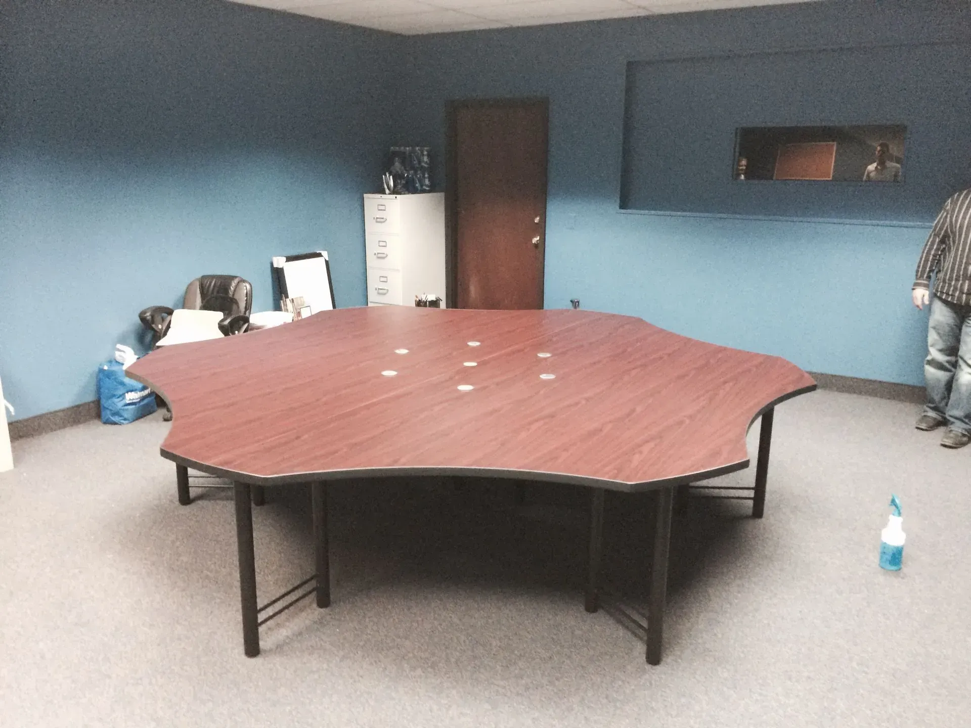 Large, ornate conference table in a room with blue walls, a door, and a person standing to the side.