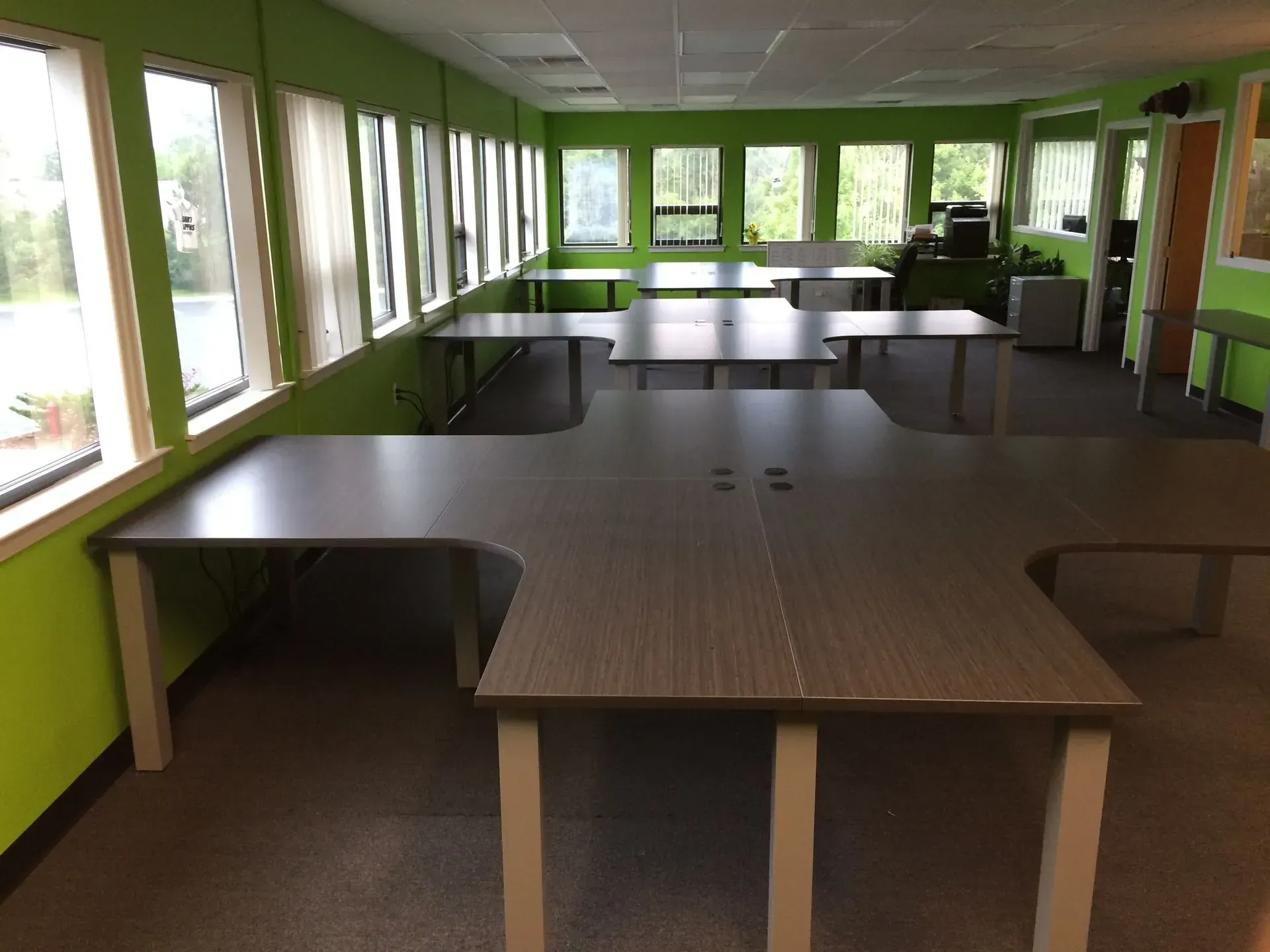 Empty office space with several gray desks, green walls, and large windows.