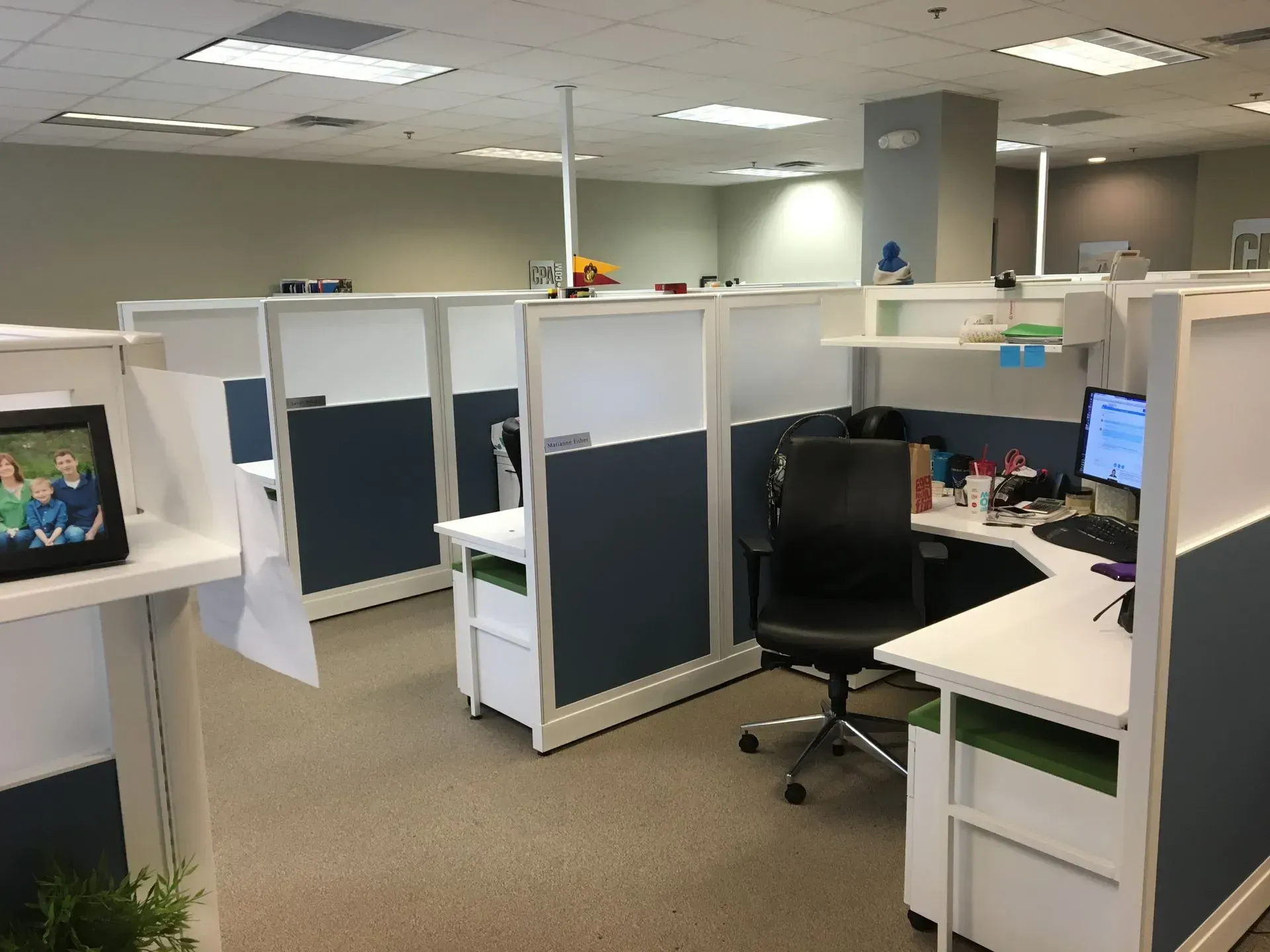 Office cubicles with gray and white walls and desks; the room has beige carpet and overhead fluorescent lighting.