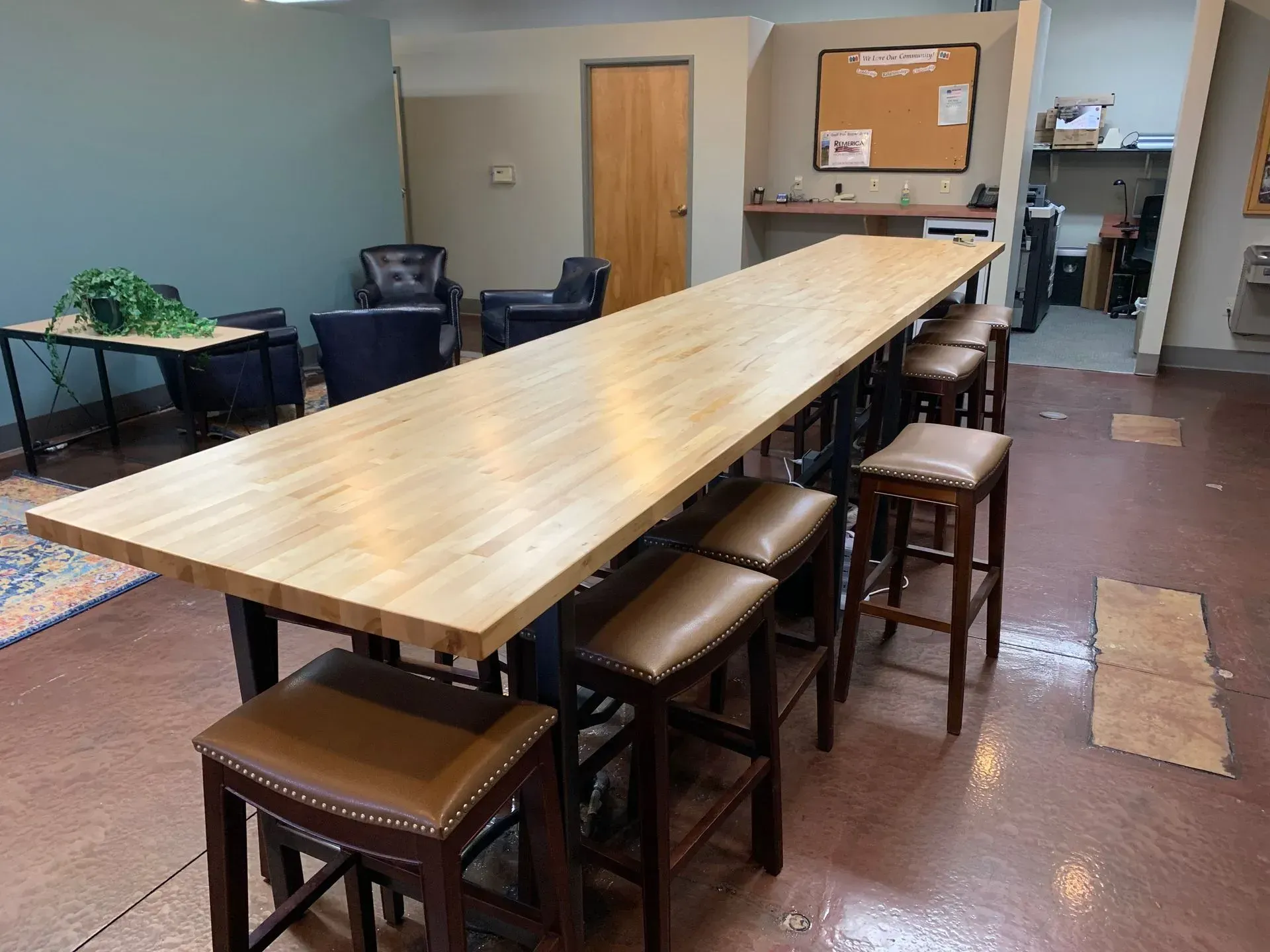 A long wooden table with brown leather bar stools in a brightly lit room.
