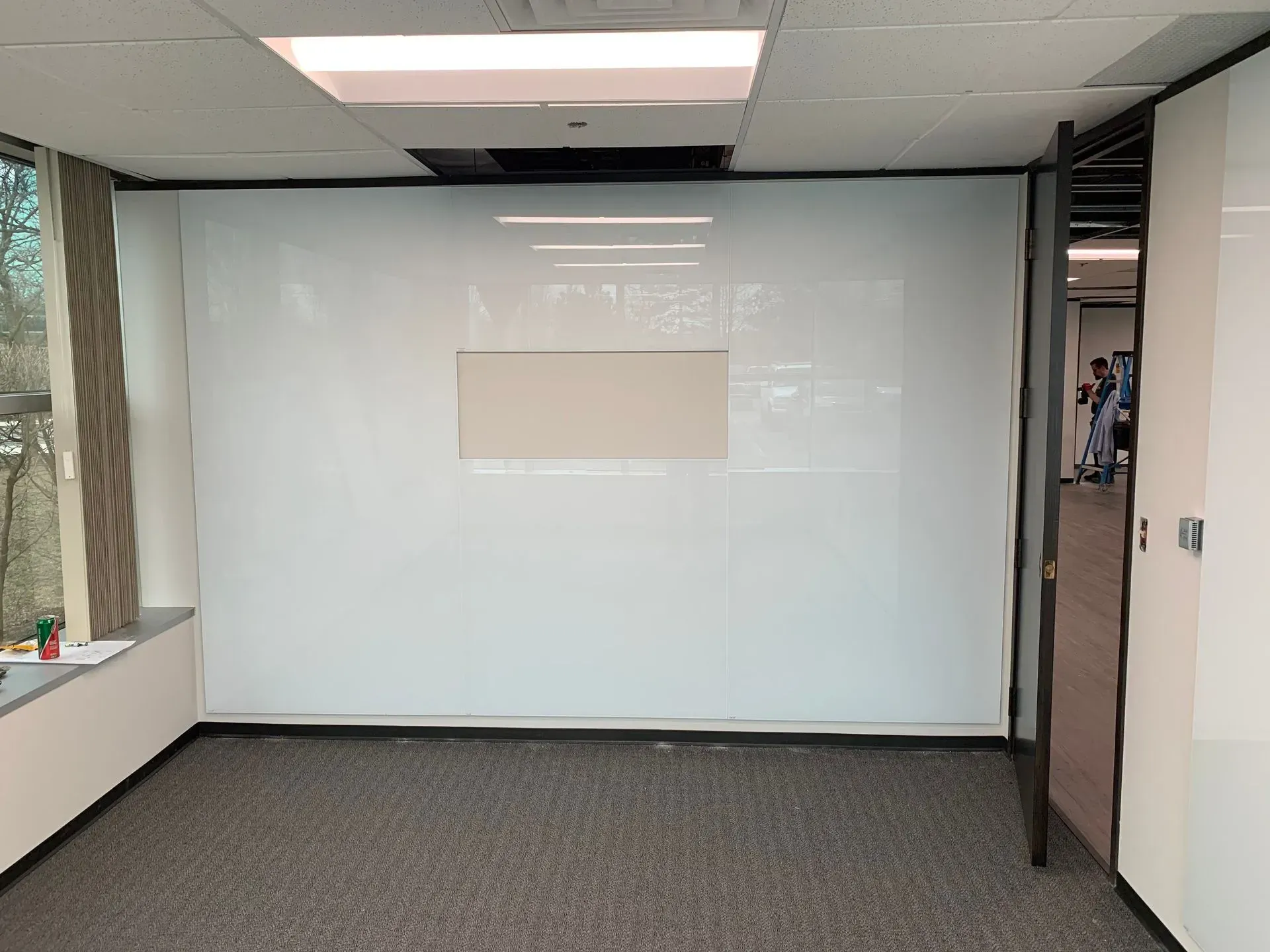 Empty office room with white walls and a brown carpet. A section of the wall has a beige panel.