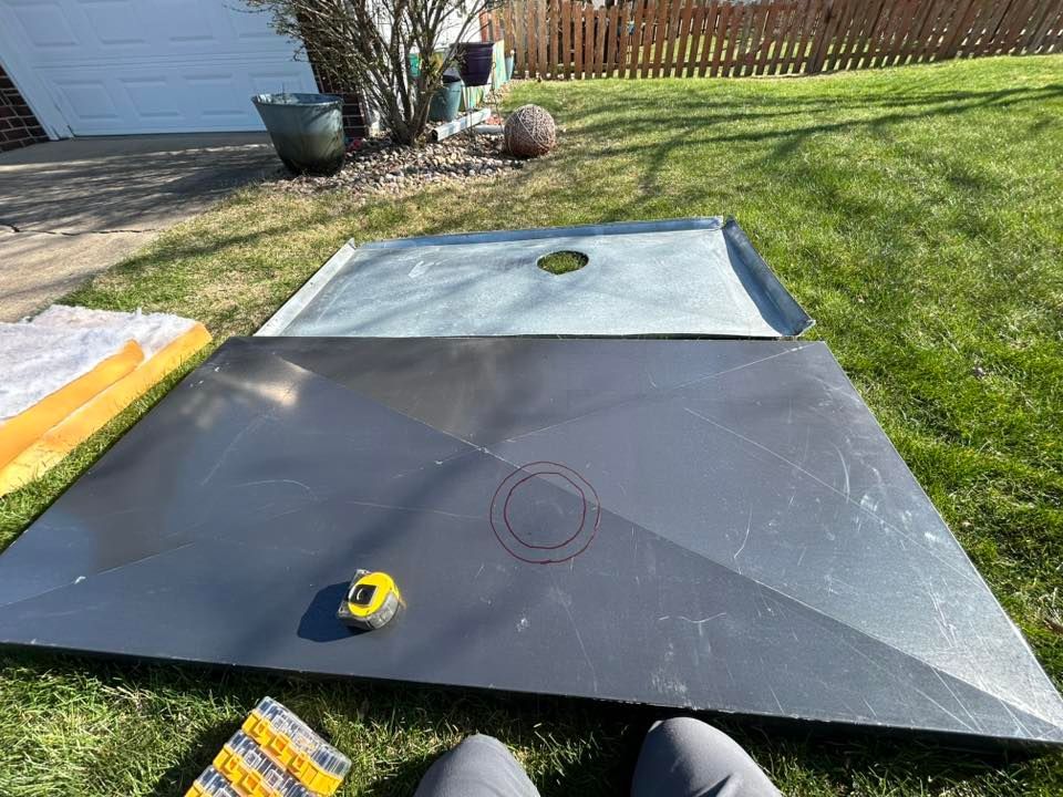 Two shower bases, one gray, one light blue, with a measuring tape on the gray one, outdoors on grass.