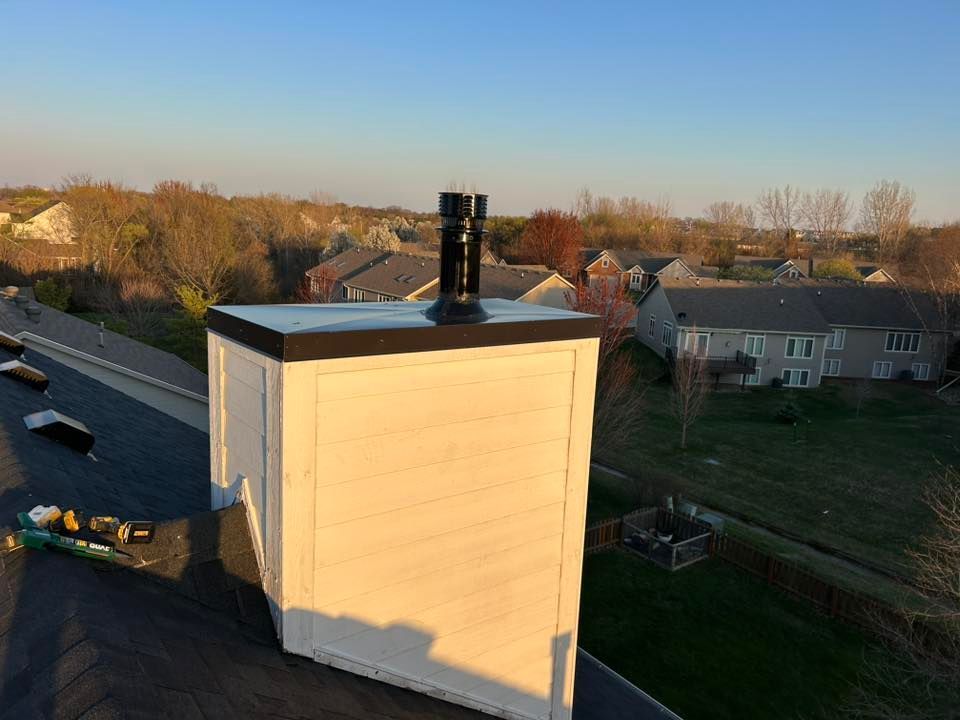 Chimney on a rooftop with a black cap and a neighborhood view.