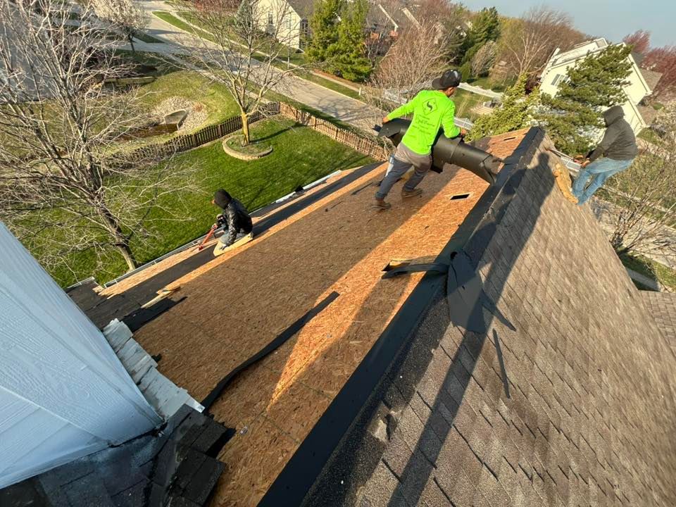 Roofers working on a shingled roof, laying down underlayment. Sunny day.
