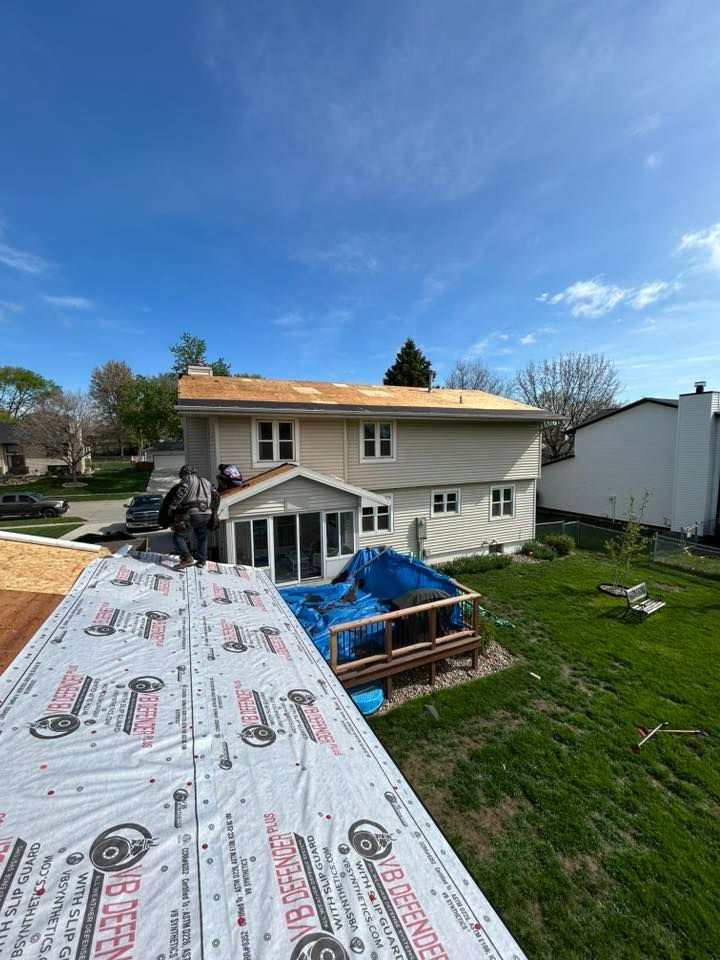 Roofers working on a two-story house with a partial roof replacement underway on a sunny day.