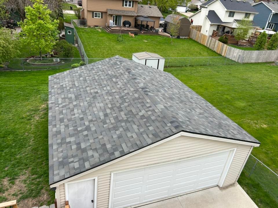 Garage roof with gray shingles, in a suburban backyard with green grass.