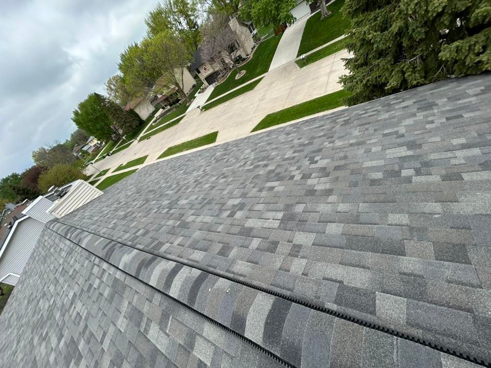 View of a gray asphalt shingle roof, with neighborhood in the background on a cloudy day.