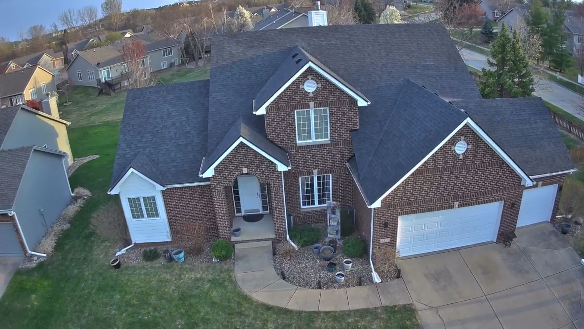 Rooftop view of a building with a dark tarp, asphalt shingles, cloudy sky, and a suburban street in the background.