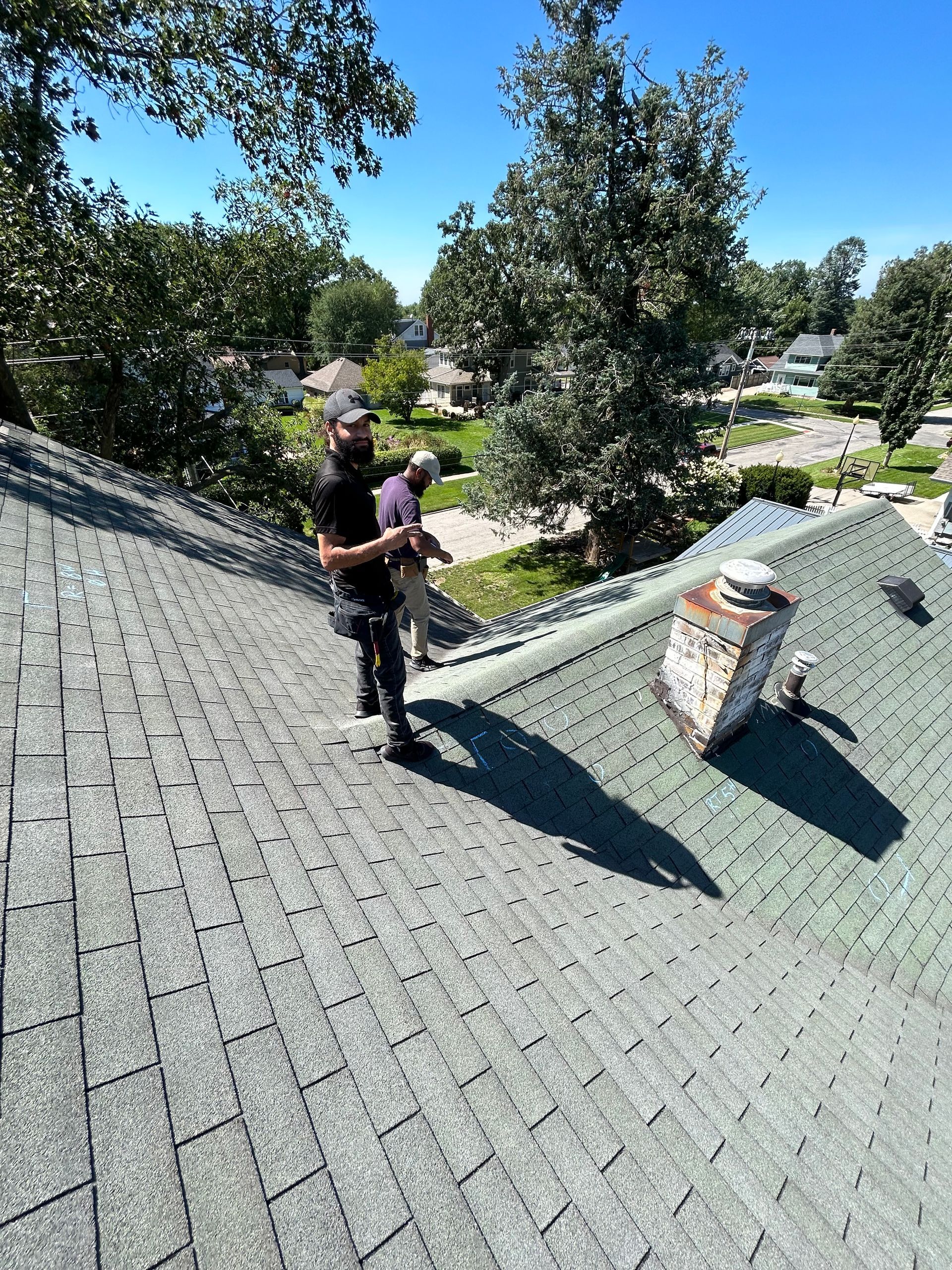 Roof with silver underlayment and old shingles partially removed, a green hose lies on the roof.