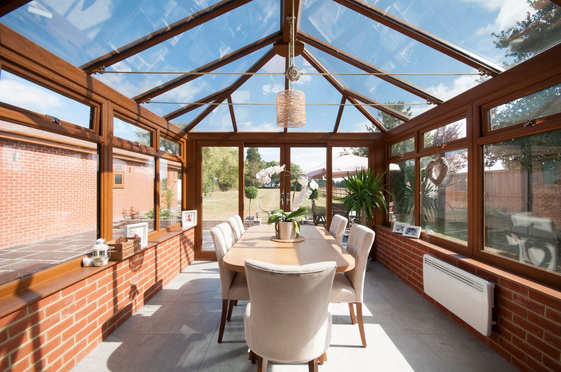 Sunroom with glass roof, brick walls, dining table, and chairs; bright, sunny day.