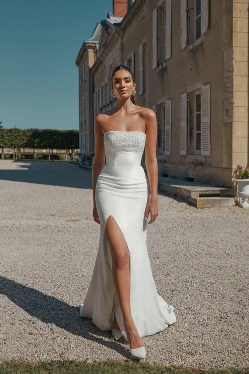 A woman in a white wedding dress is standing in front of a building.