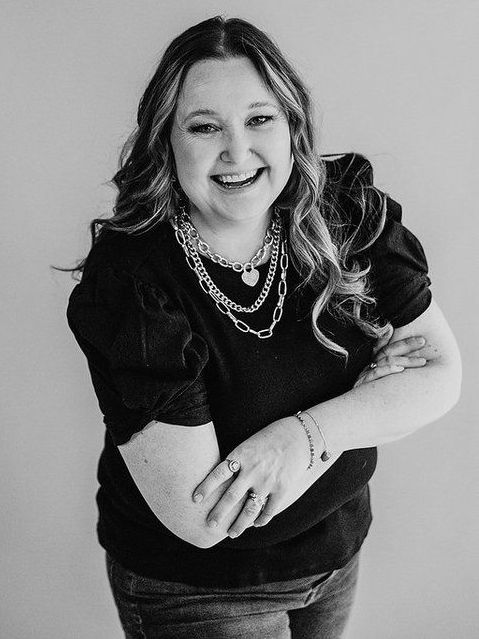 A woman wearing a black shirt and a necklace is smiling in a black and white photo.