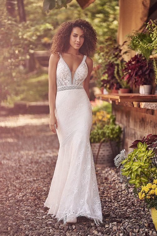 A woman in a white lace wedding dress is standing in a garden.