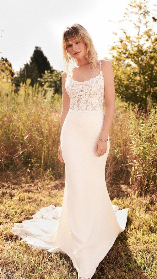 A woman in a white wedding dress is standing in a field.