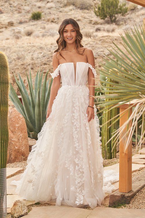 A woman in a white wedding dress is standing in front of a cactus.