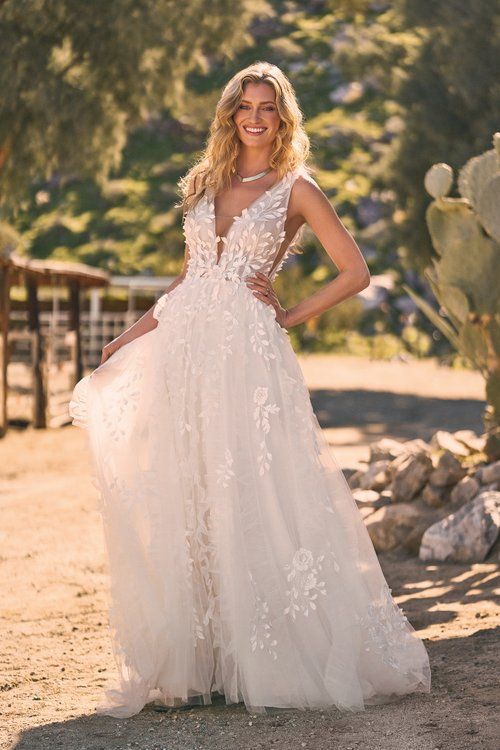 A woman in a white wedding dress is standing in front of a cactus.