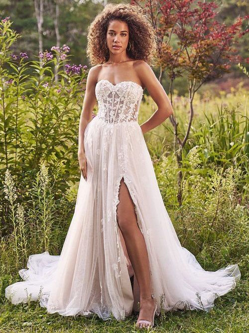 A woman in a white wedding dress is standing in a field.