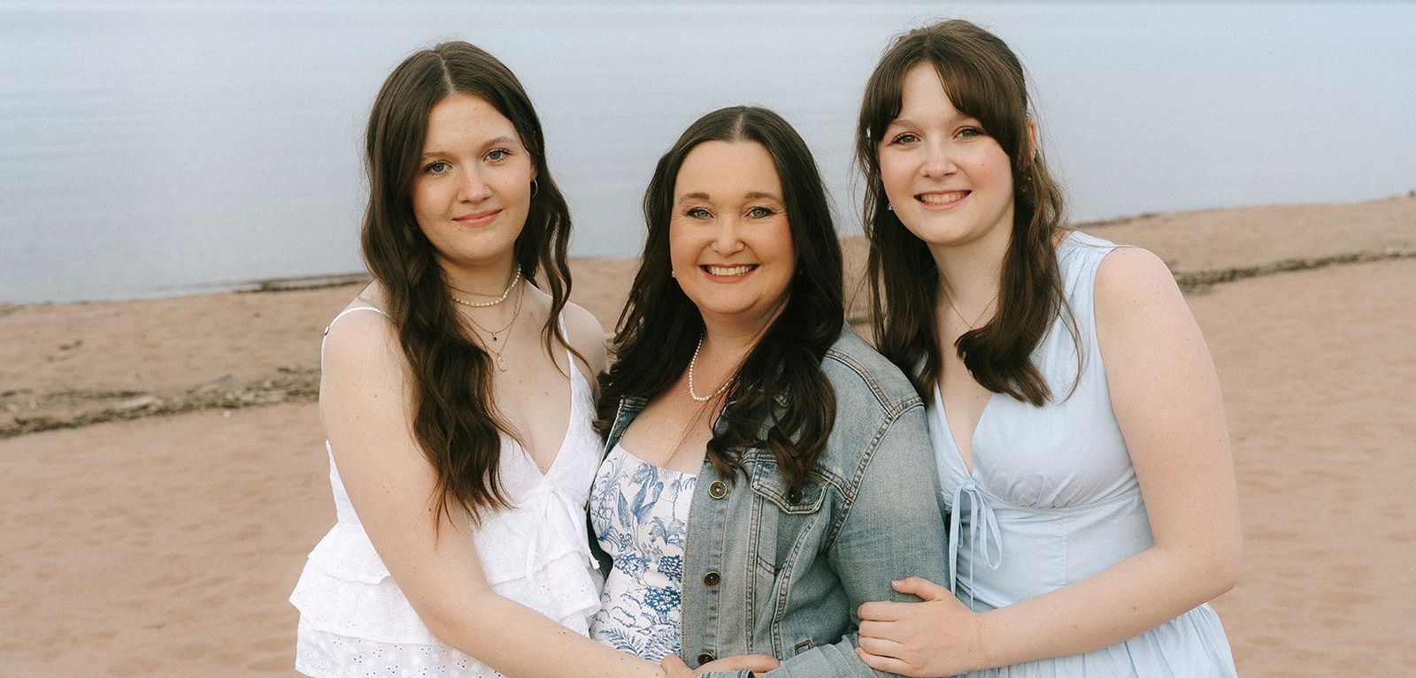 Three women are standing next to each other in front of a brick wall.