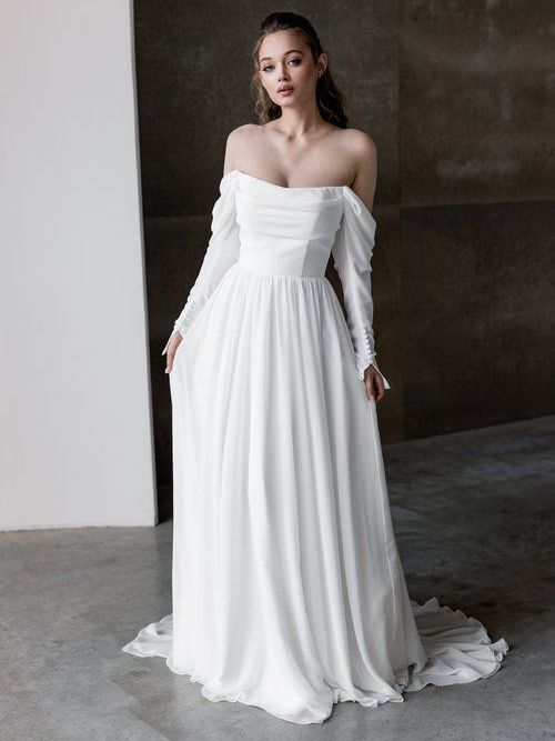 A woman is wearing a white wedding dress with long sleeves.