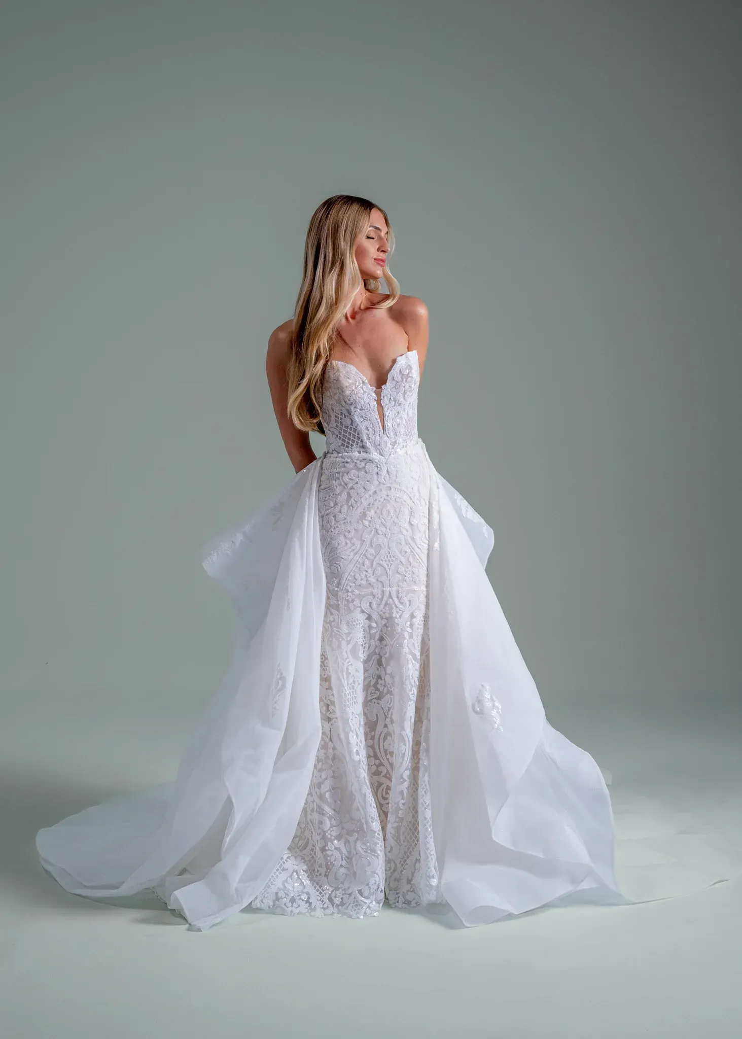 A woman in a white wedding dress is standing in front of a brick building.
