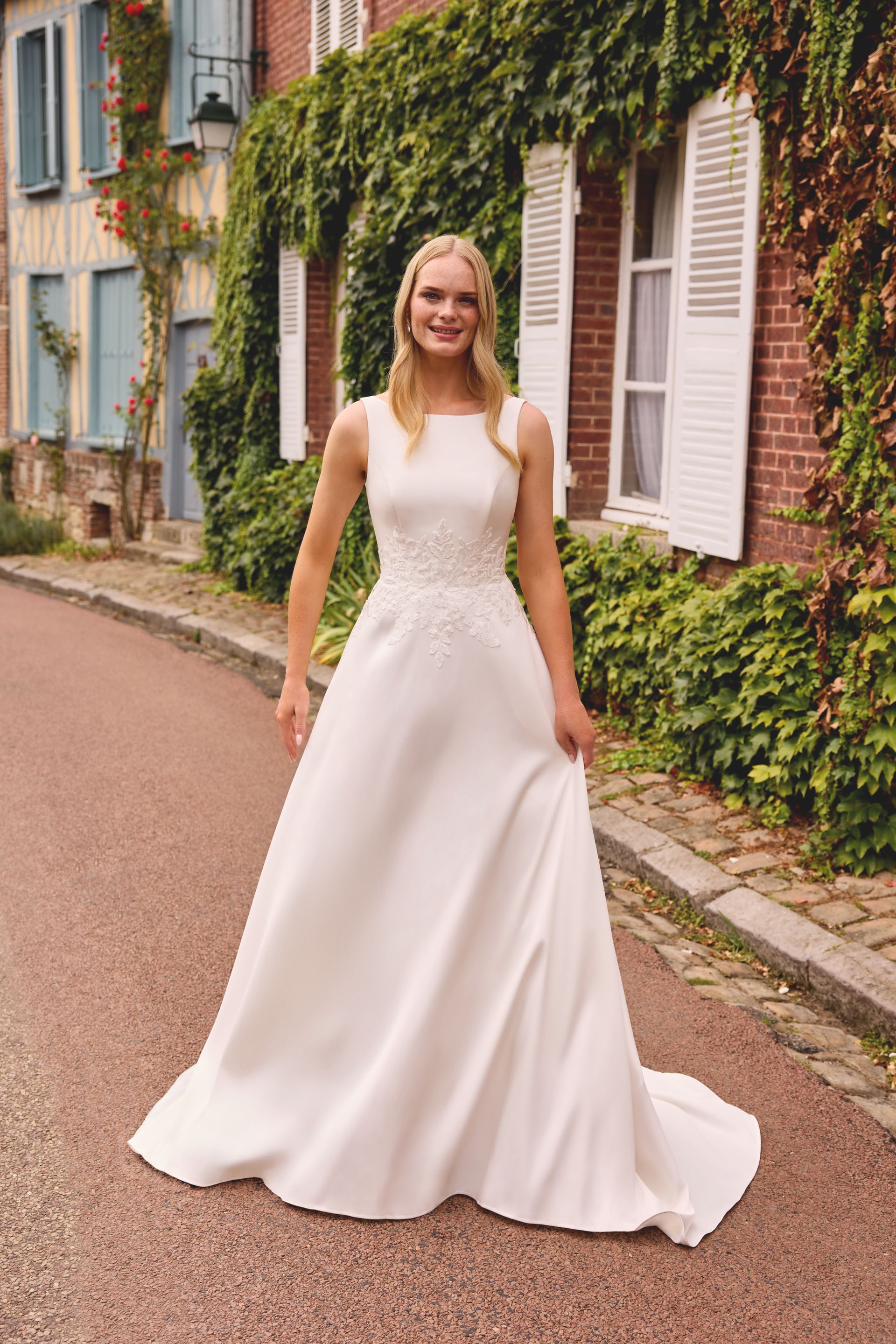 Woman in white strapless wedding dress with slit, standing in a garden with flowers.