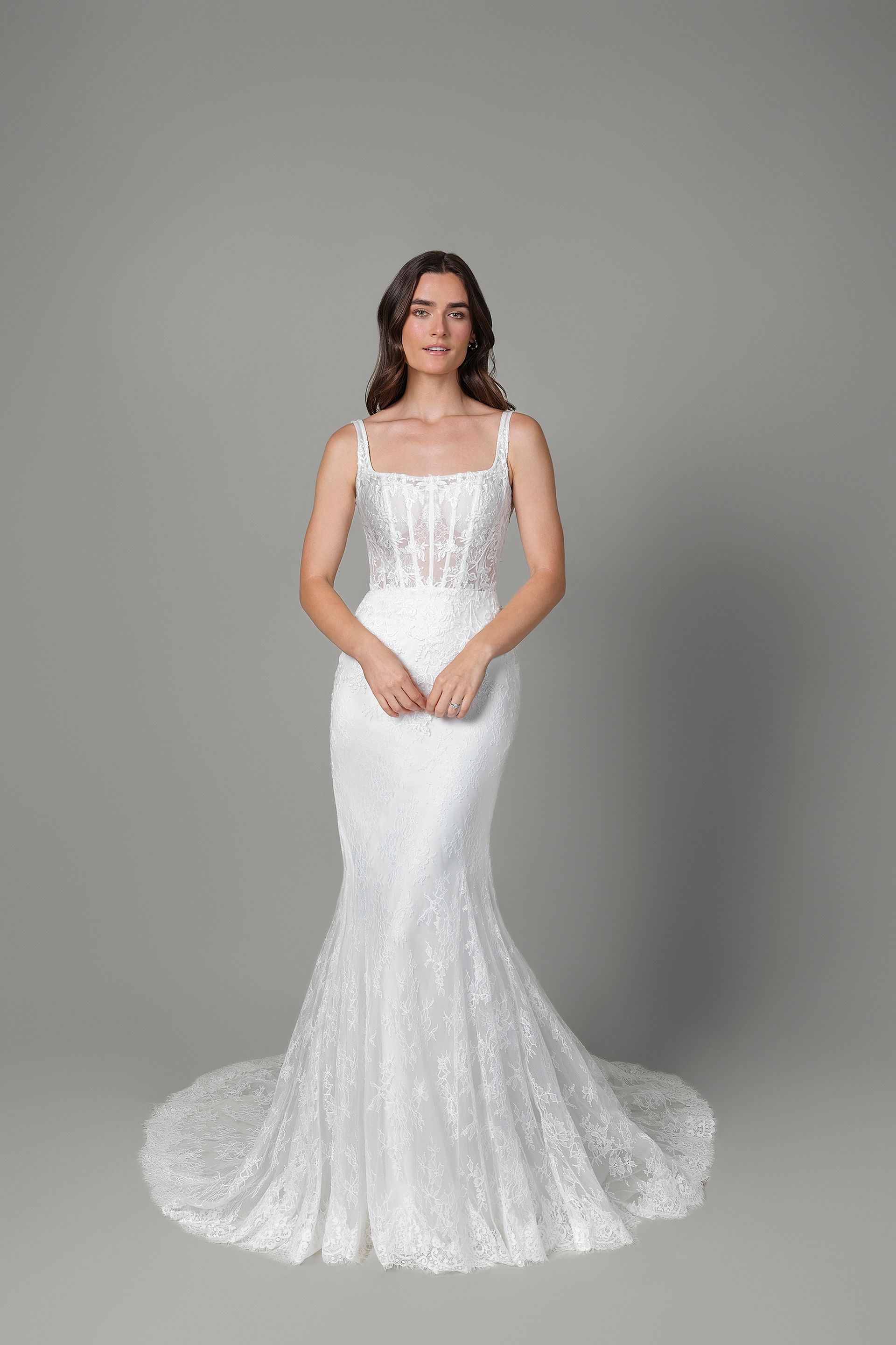 Woman in a white sequined mermaid wedding dress with lace bodice, standing, smiling, on a gray backdrop.
