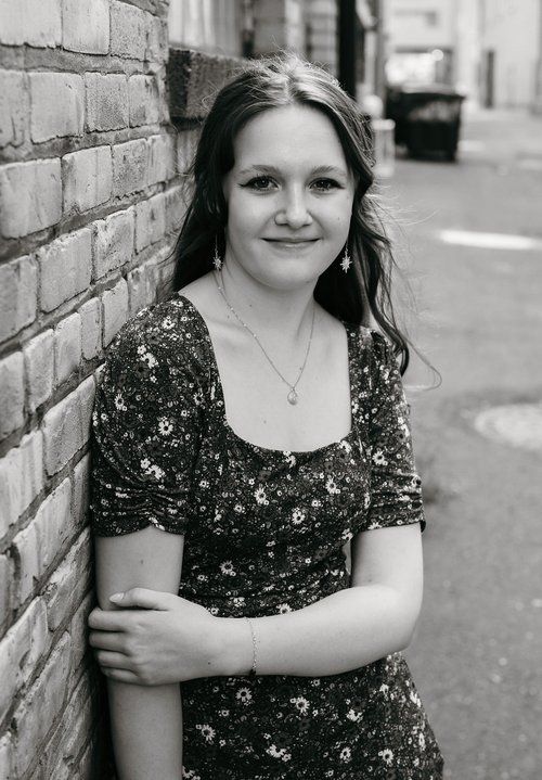 A woman is leaning against a brick wall in a black and white photo.
