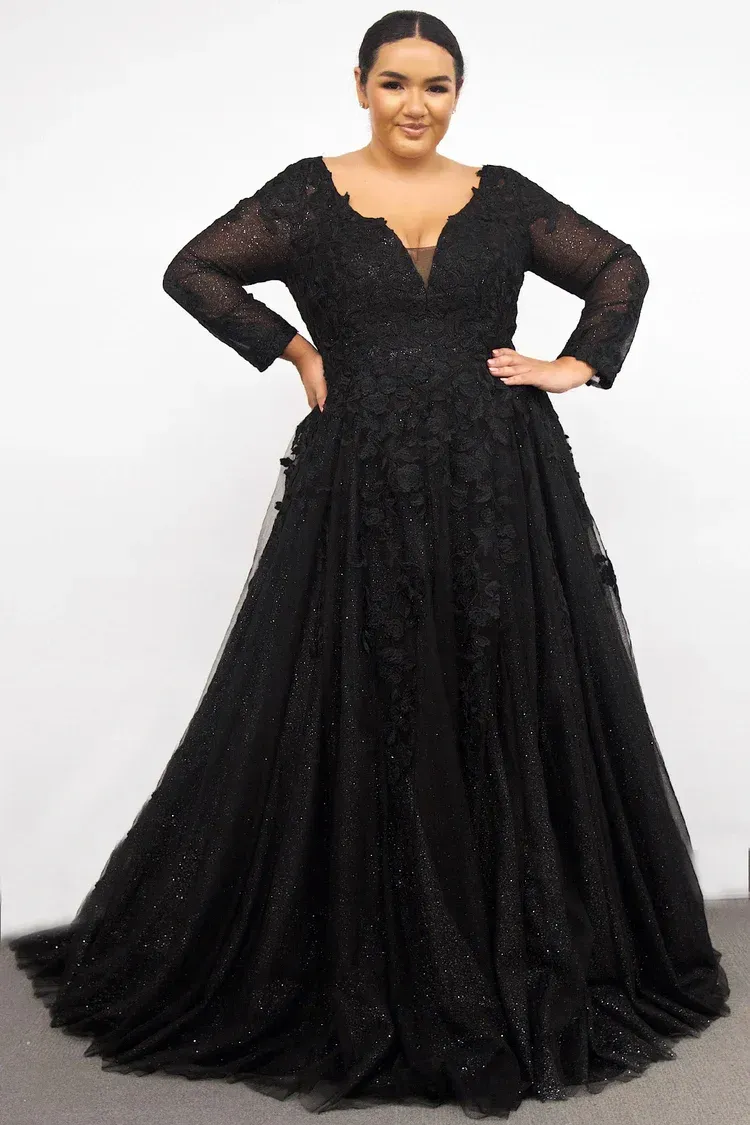 Woman in long black formal gown, hands on hips, smiling.