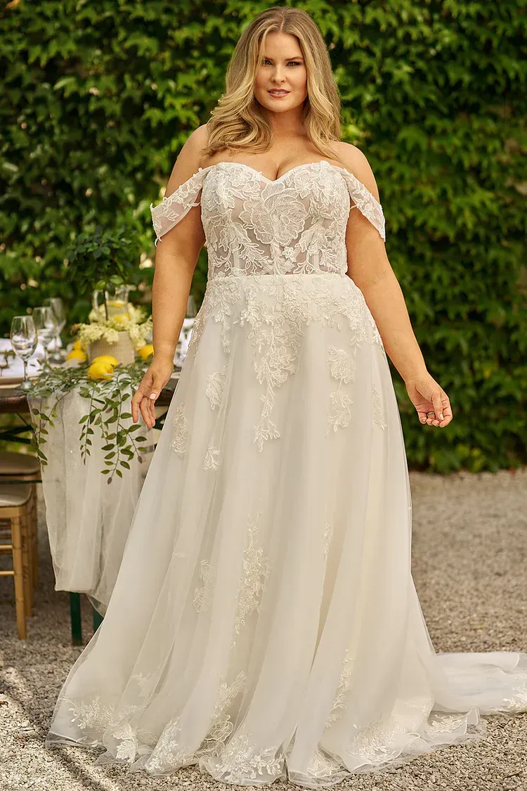 Woman in a white off-the-shoulder wedding dress, standing outdoors.