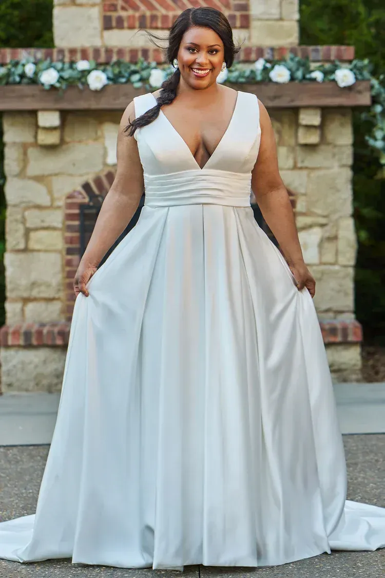 Woman in a white wedding dress smiles, standing outdoors in front of a stone fireplace.