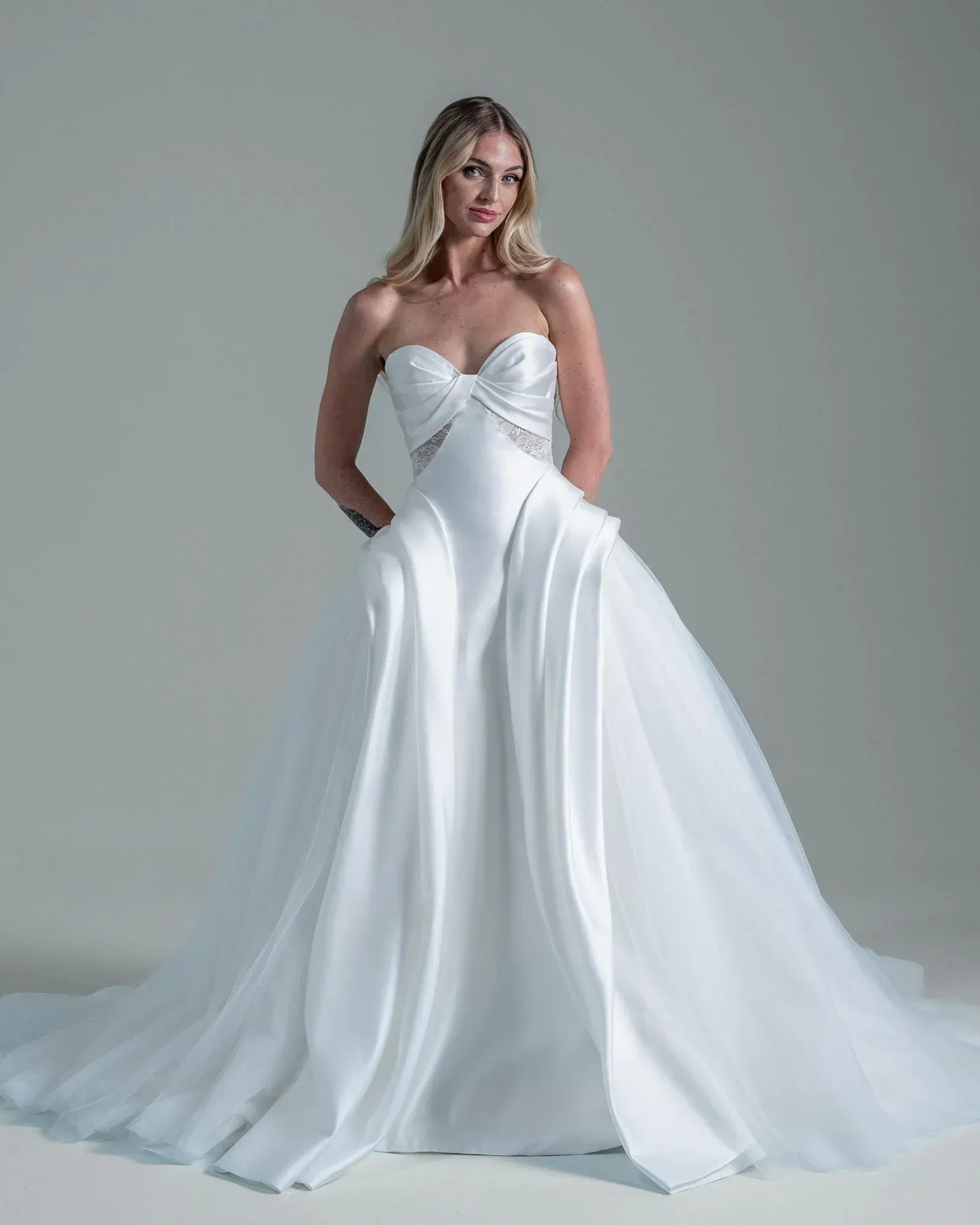 A woman is wearing a white off the shoulder wedding dress with a high slit.