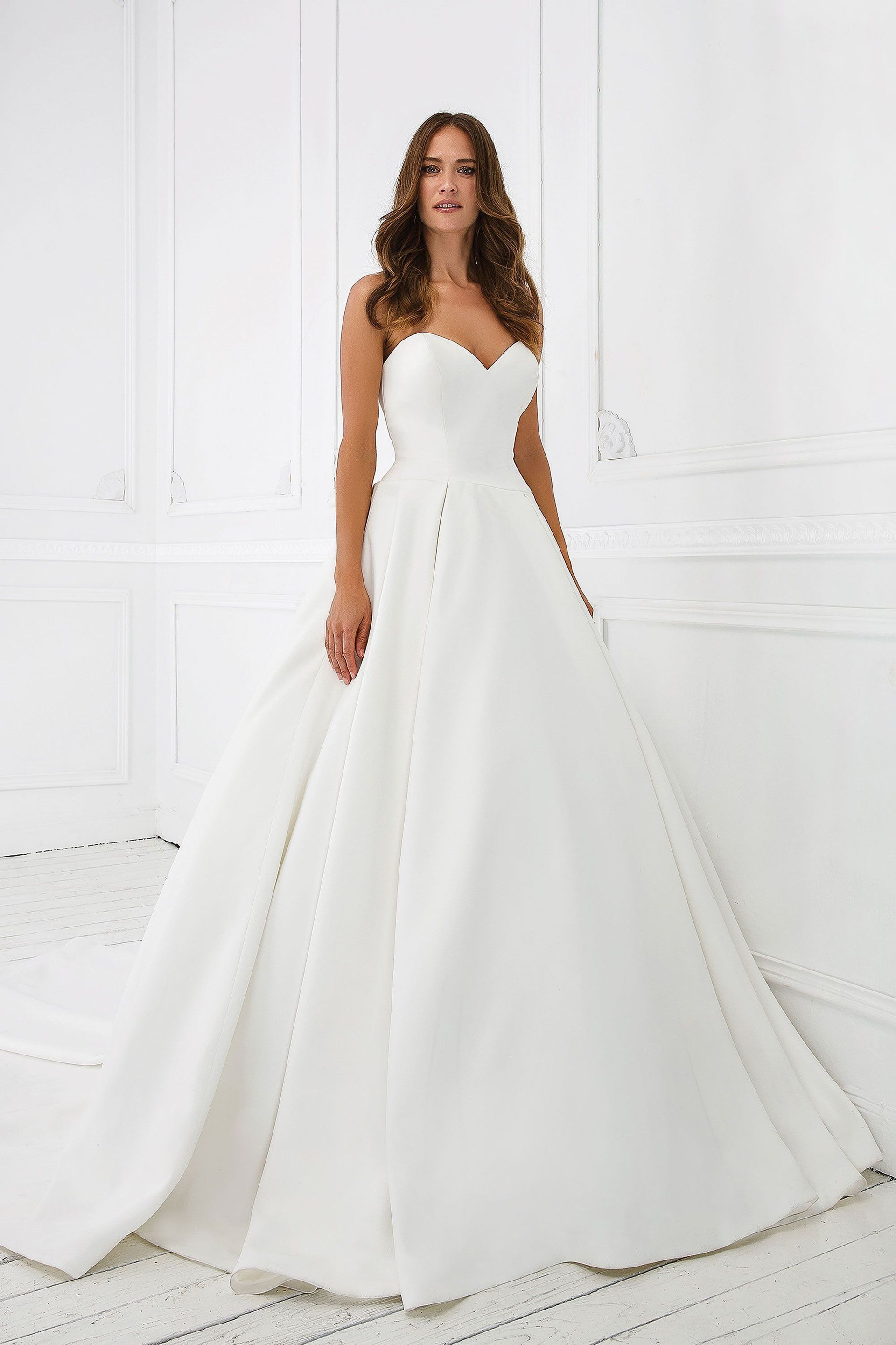 A woman in a white wedding dress is standing in front of a white wall.
