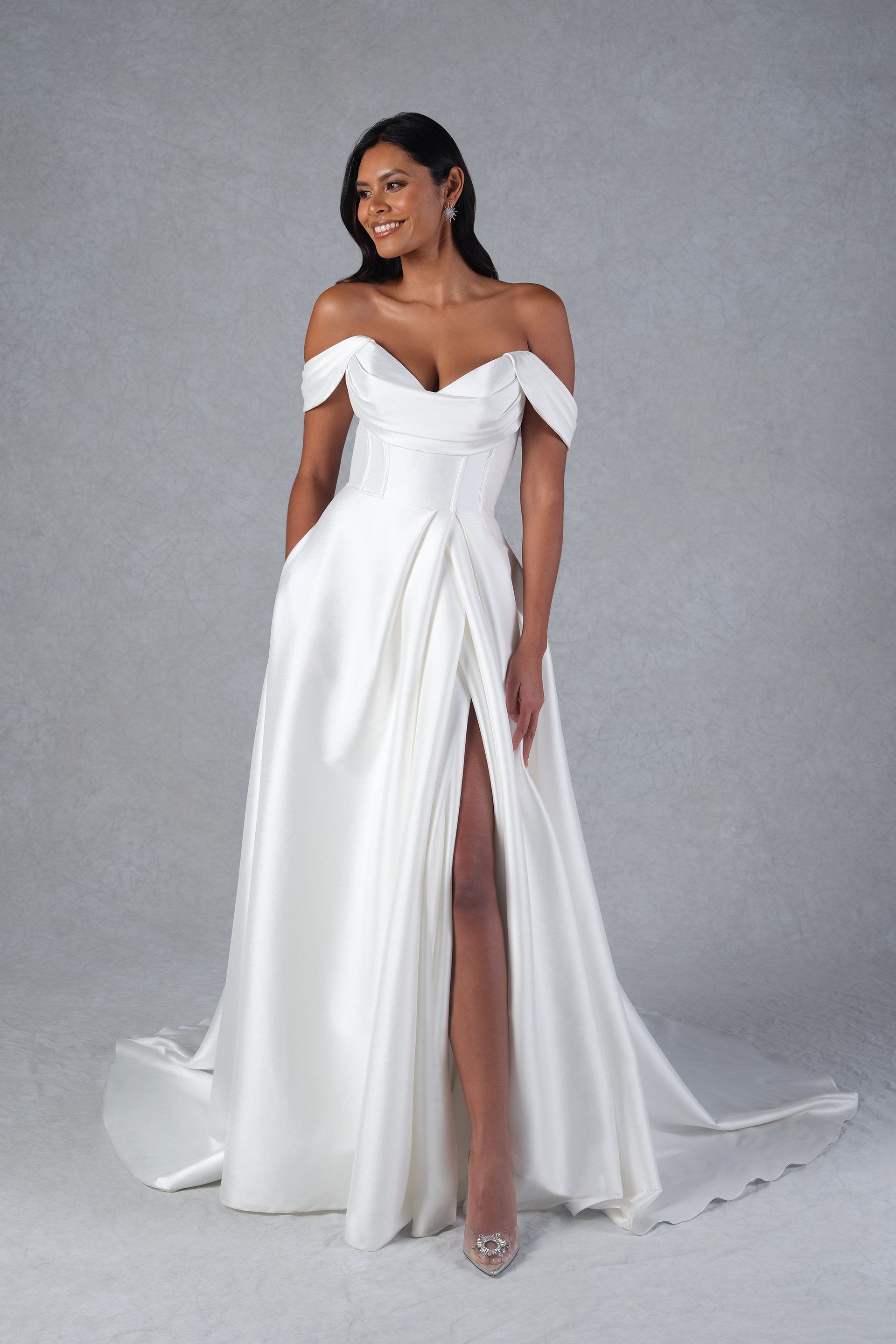 A woman is wearing a white off the shoulder wedding dress with a high slit.