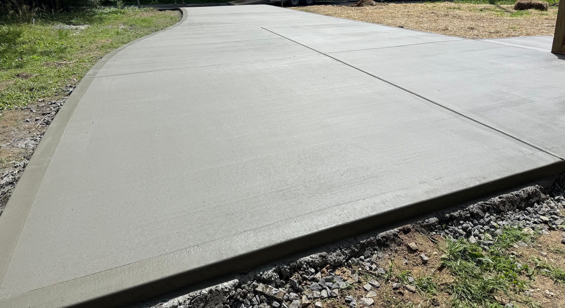 Newly poured concrete driveway. Gray surface with gravel border.