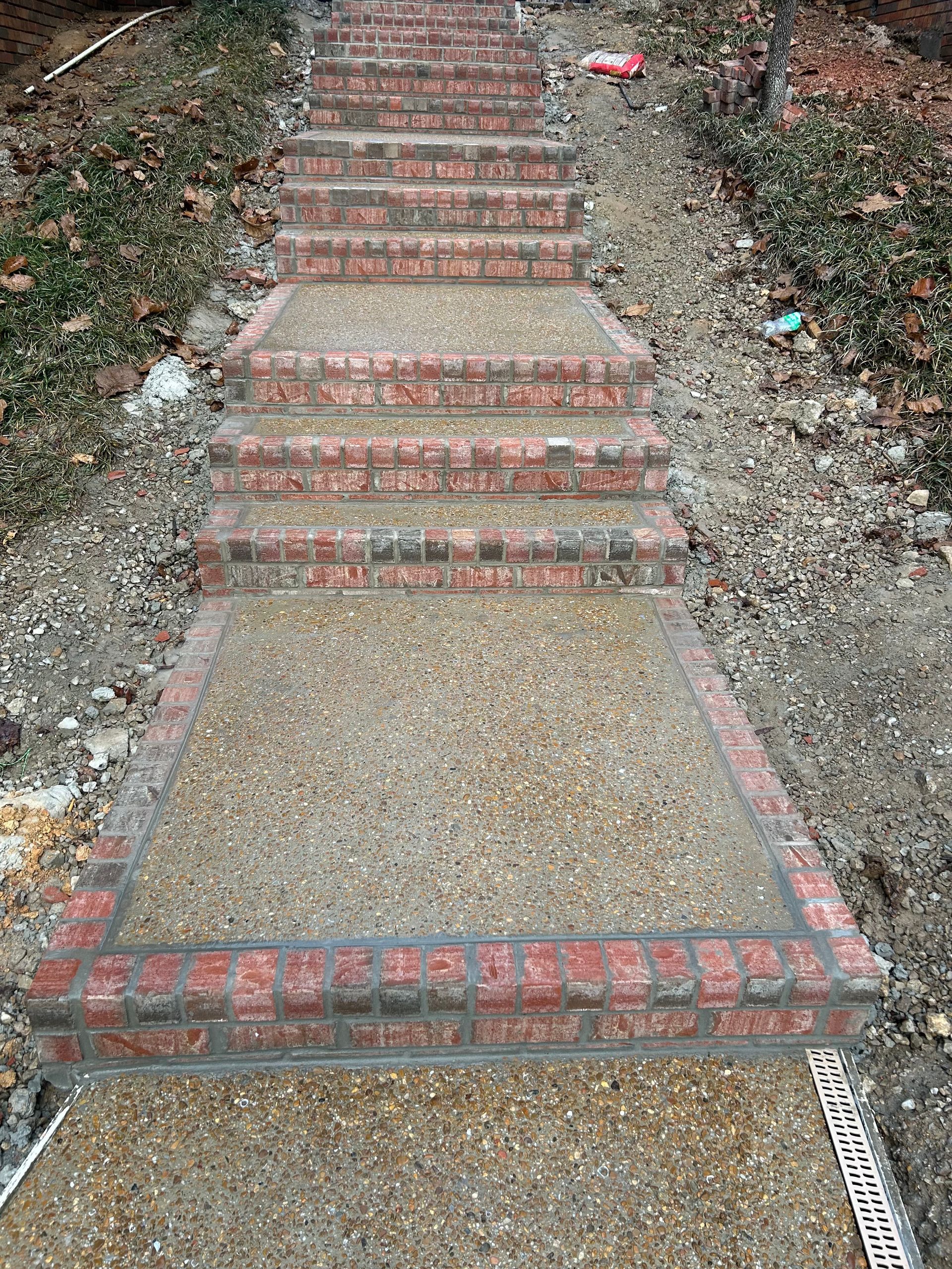 Brick steps with exposed aggregate surface, edged in brick, leading uphill.