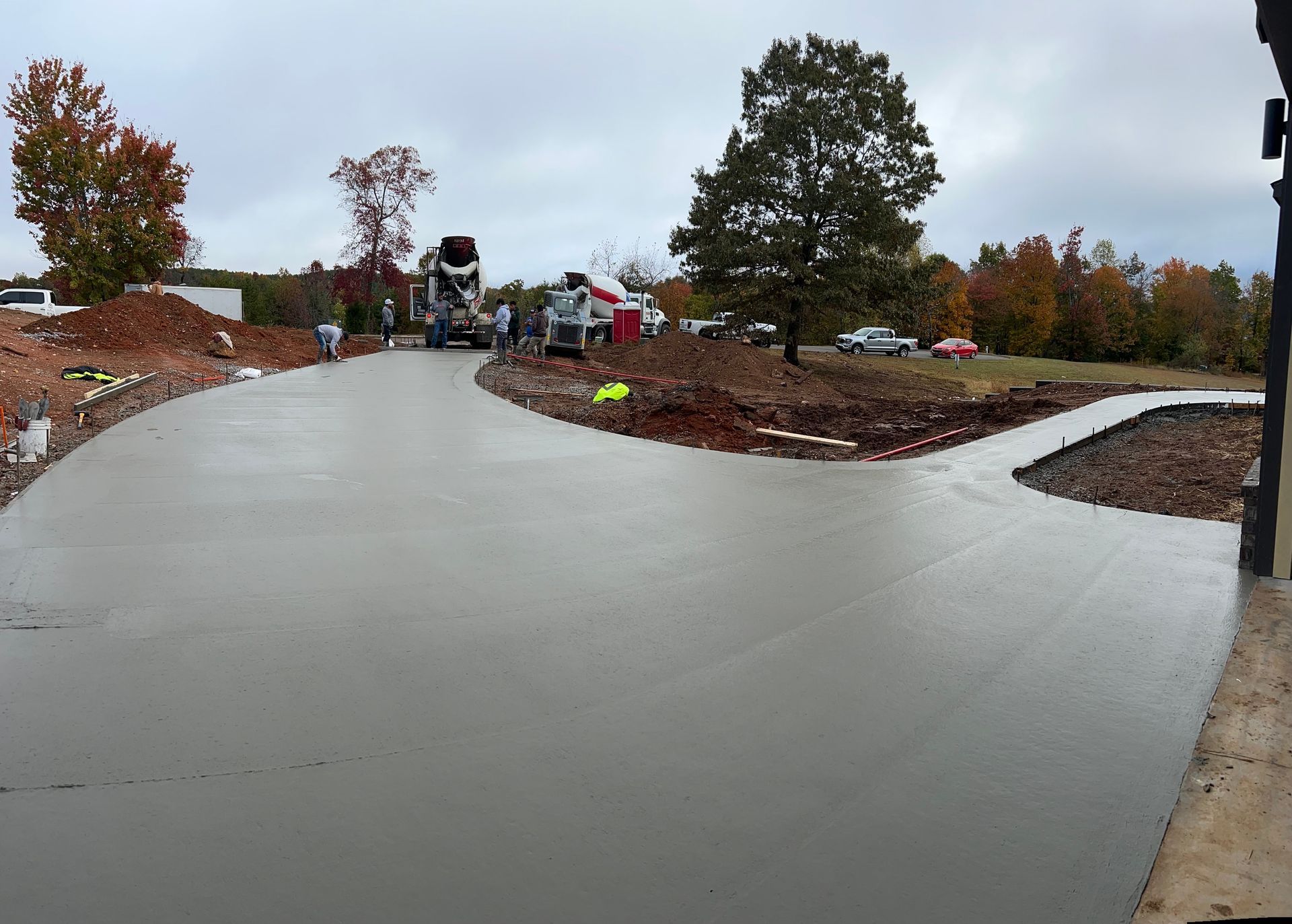 Freshly poured concrete driveway under overcast sky; construction equipment and trees in the background.