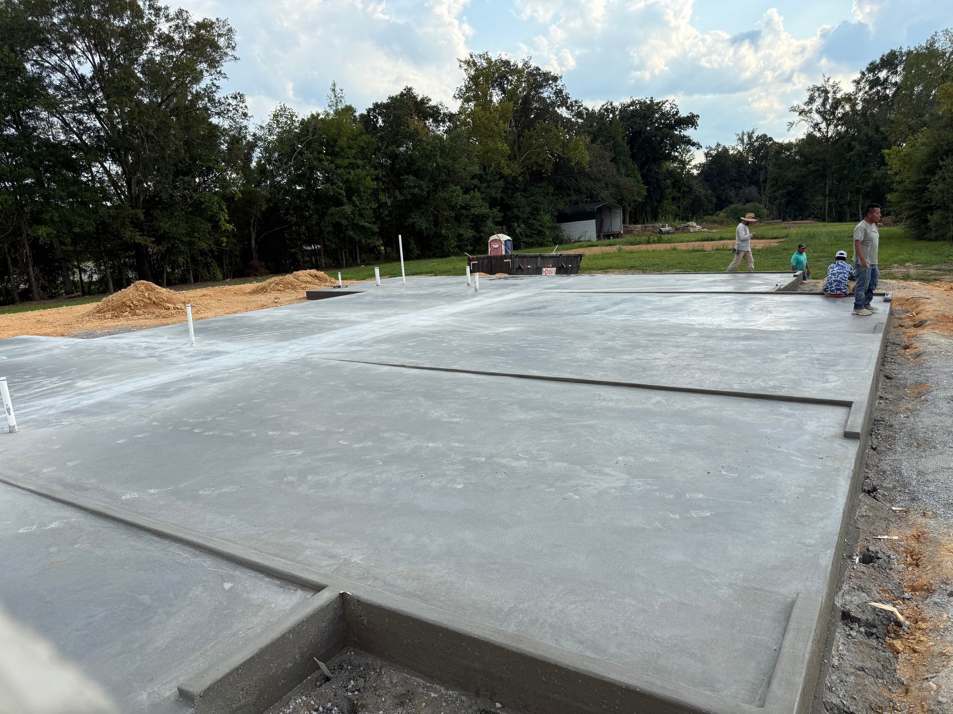 Newly poured concrete foundation with workers in background, construction site.