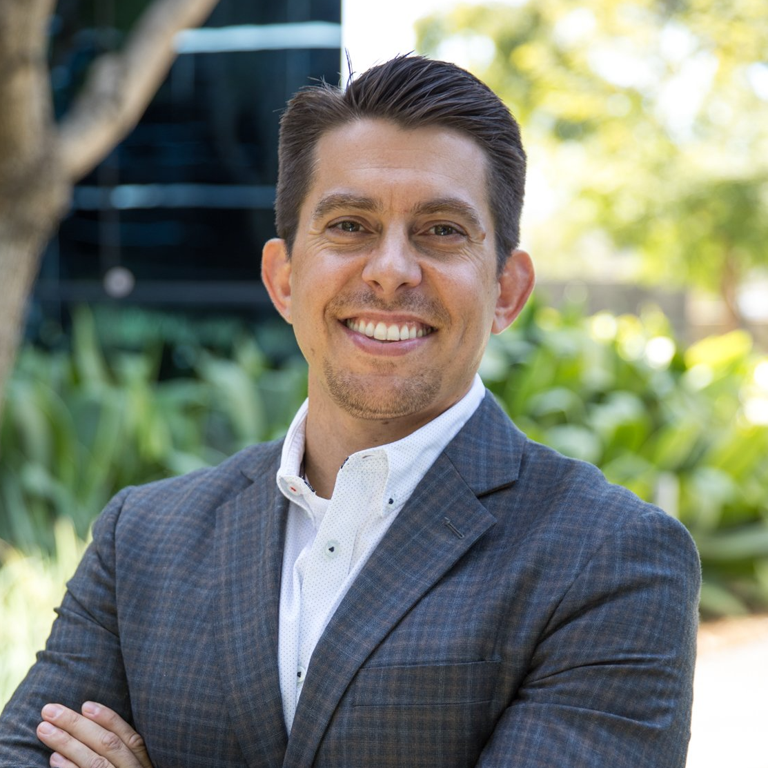 A man in a suit and white shirt is smiling with his arms crossed.