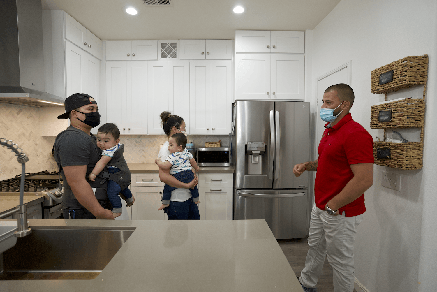 A man wearing a mask talks to a family in a kitchen