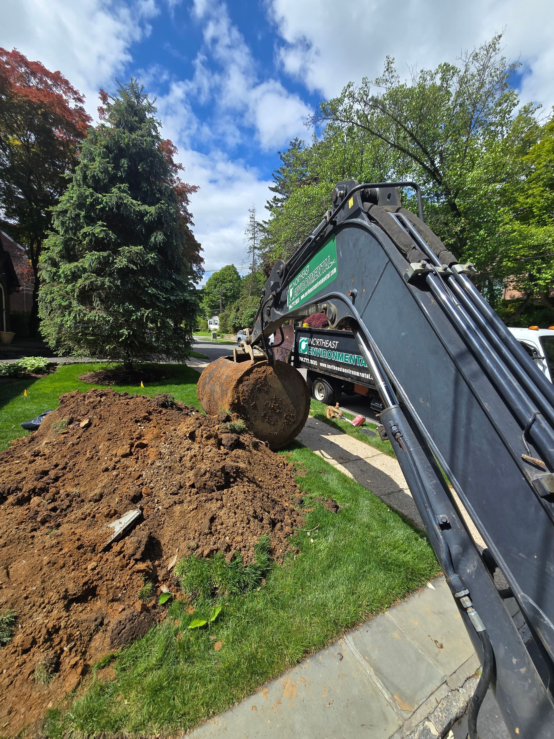 Excavator arm lifting a dirt clump beside a landscaped lawn under a blue sky